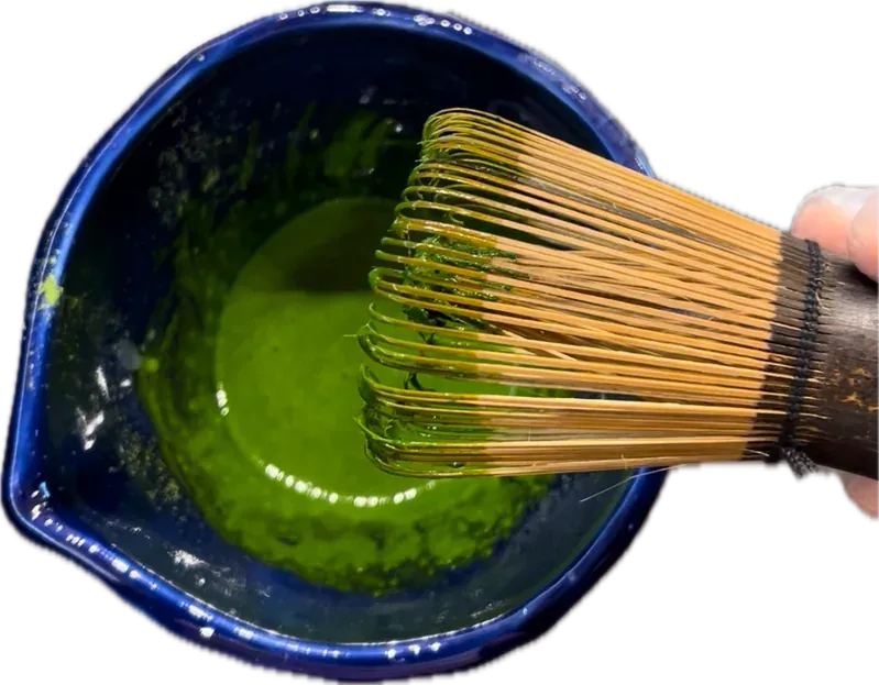 Un chasen de bambú batiendo matcha en un chawan azul